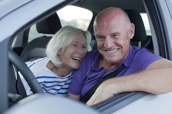 An elderly couple sitting in a car, smiling and looking relaxed, suggesting confidence and happiness with their driving abilities